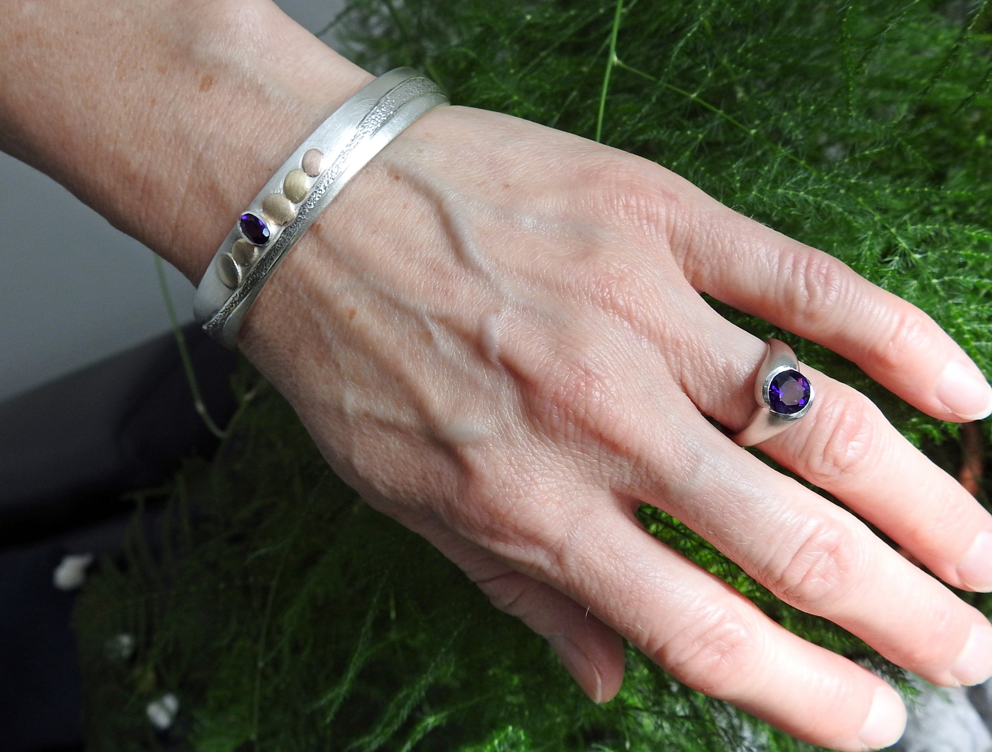 sterling silver with 14kt yellow and red gold pebbles and 18kt yellow gold pebble, with 6x4mm oval facetted amethyst set in sterling silver bezel, hand carving and planish detailing.  bracelet by ZEALmetal, Nicole Horlor, in Kingston, ON Canada