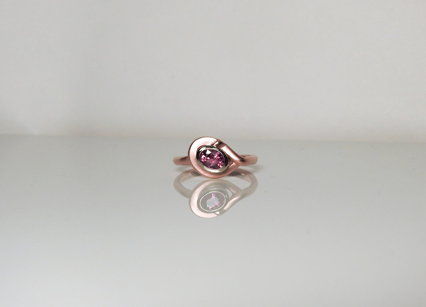 Soft red gold rounded ring, wrapping around a heavy white gold bezel, set with a glowing oval ruby, by ZEALmetal, Nicole Horlor, in Kingston, ON Canada