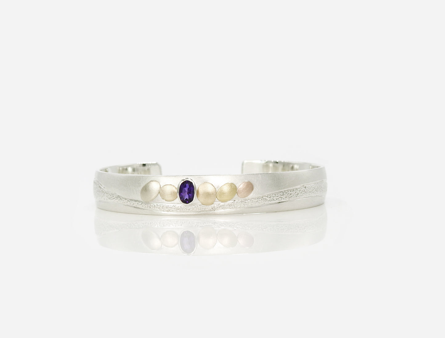 sterling silver with 14kt yellow and red gold pebbles and 18kt yellow gold pebble, with 6x4mm oval facetted amethyst set in sterling silver bezel, hand carving and planish detailing. bracelet by ZEALmetal, Nicole Horlor, in Kingston, ON Canada