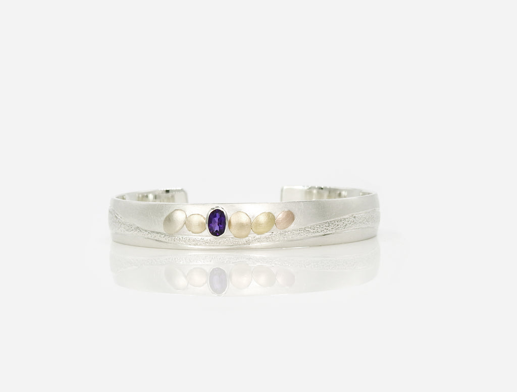 sterling silver with 14kt yellow and red gold pebbles and 18kt yellow gold pebble, with 6x4mm oval facetted amethyst set in sterling silver bezel, hand carving and planish detailing.  bracelet by ZEALmetal, Nicole Horlor, in Kingston, ON Canada